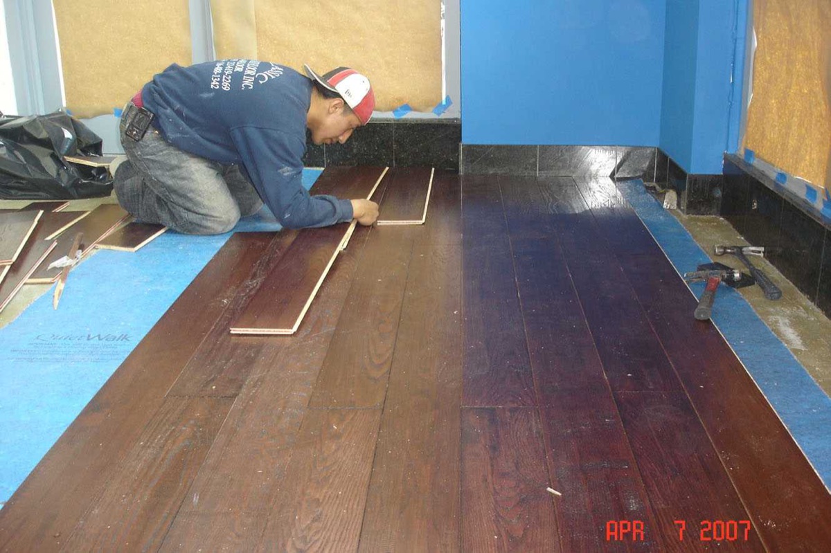 Technician laying wide dark hardwood planks